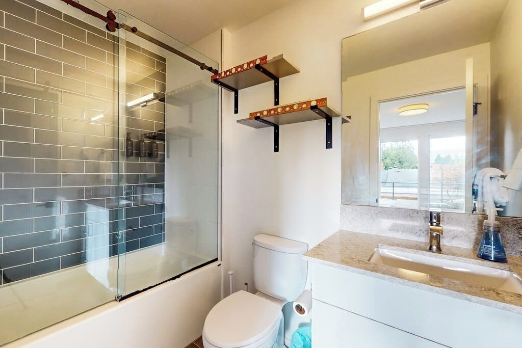 Un bagno con box doccia in vetro, un WC, un lavabo con specchio sopra e un porta asciugamani.