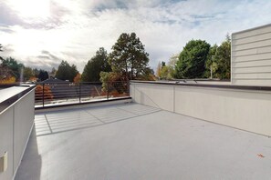 A rooftop terrace with a metal railing, trees in the background, and a clear sky. - 3 BR townhome with rooftop deck and city access (Seattle)