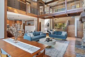 A spacious living area with a high ceiling, a dining table, and a blue sofa set. - 4BR mountain-view house withhome office & fireplace (Cle Elum)