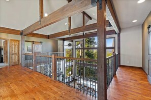 A spacious room with wooden beams, a balcony with a metal railing, and large windows. - 4BR mountain-view house withhome office & fireplace (Cle Elum)