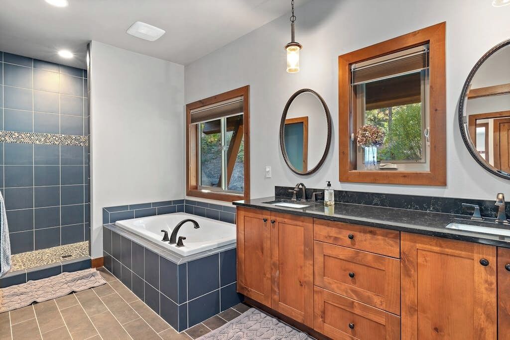 Een moderne badkamer met een ruim bad, een houten wastafelmeubel en meerdere spiegels.