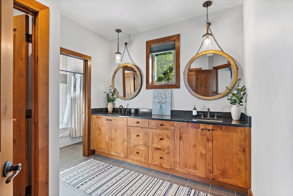 Une salle de bain moderne avec des meubles en bois, un plan de travail noir et trois miroirs ronds.
