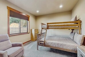 Quarto com beliche, cabeceira de madeira, uma cama de solteiro, uma cadeira e janela com persianas.