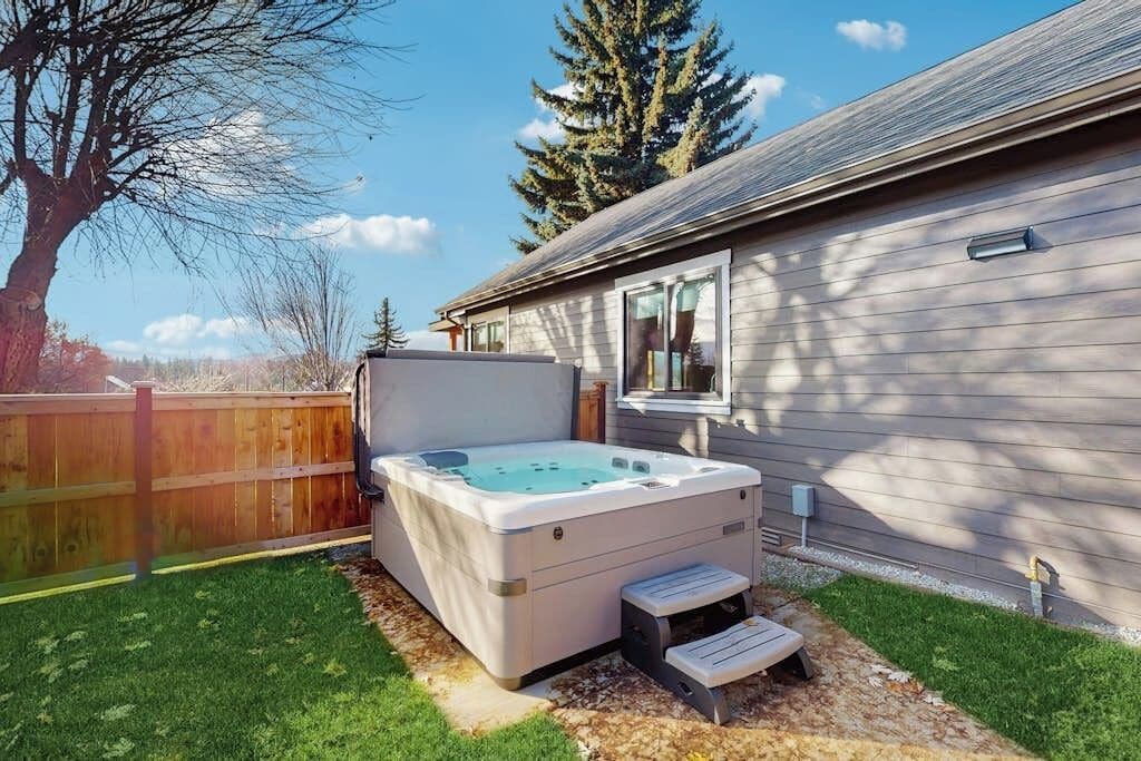 A hot tub in a backyard with a wooden fence and a house in the background.