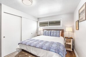 A bedroom with a bed, bedside lamps, a window, and a door.