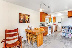 A kitchen with wooden cabinets, a dining table with chairs, a refrigerator, and a bookshelf.