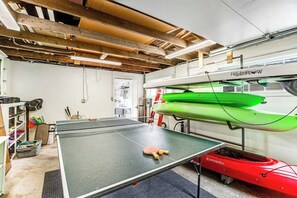 A ping pong table in a room with a high ceiling, wooden beams, and a green kayak on a stand.