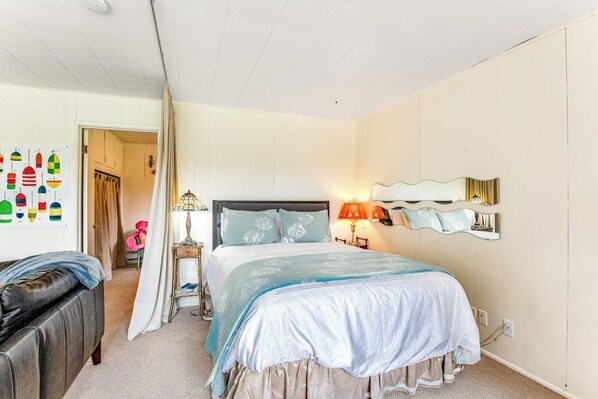 A bedroom with a bed, bedside table, lamp, and a wall-mounted mirror.