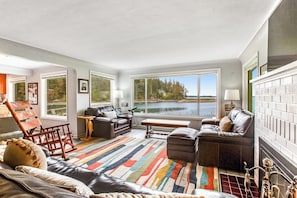 A spacious living room with a large window overlooking a lake, furnished with leather sofas and a colorful rug.