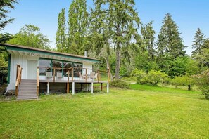 A modern house with a deck, surrounded by a grassy yard and tall trees.