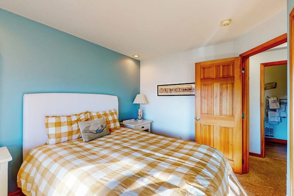 A bedroom with a checkered bedspread, a nightstand with a lamp, and a door leading to another room.