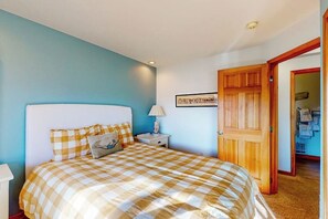 Een slaapkamer met een geruite sprei, een nachtkastje met een lamp, en een deur naar een andere kamer.
