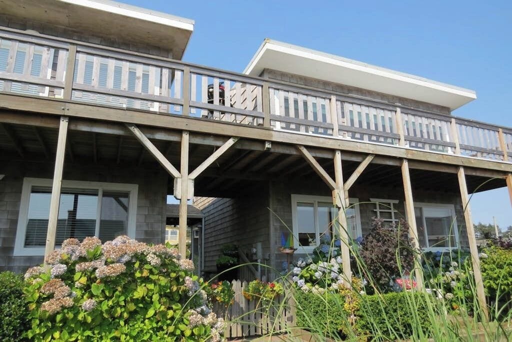 Een gebouw met twee verdiepingen, een balkon, houten balken en een tuin met diverse planten.