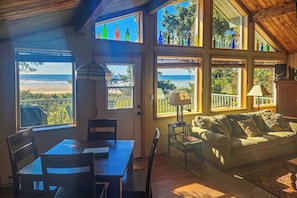 Een kamer met een eettafel en stoelen, een bank en grote ramen met uitzicht op het strand.