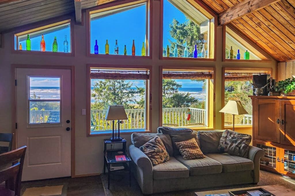 A cozy living room with a sofa, a lamp, and a view of the sea through large windows.