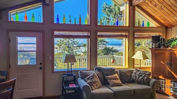 A cozy living room with a sofa, a lamp, and a view of the sea through large windows.