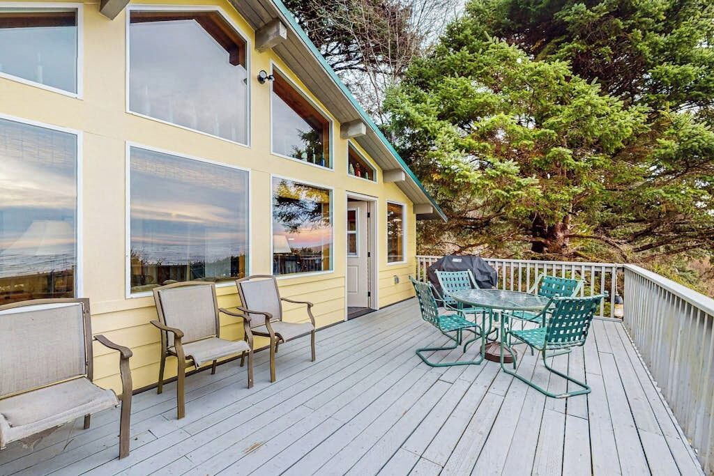 A wooden deck with outdoor seating, a covered area, and a view of a tree and landscape.