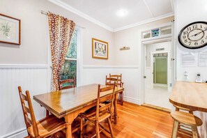 A dining area with a wooden table and chairs, a clock on the wall, and a door labeled 'ETIKIM'. - Restored 3BR Dog Friendly - Deck - Firepit - Washer Dryer (Sequim)