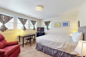 Ein Hotelzimmer mit einem Bett, einem Schreibtisch, einem Sessel, einem Fernseher und zwei gerahmten Bildern an der Wand.