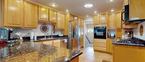 A kitchen with wooden cabinets, granite countertops, stainless steel appliances, and recessed ceiling lights.