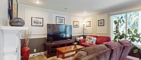 A living room with a flat-screen TV, a red sofa, a coffee table, and framed pictures on the wall.