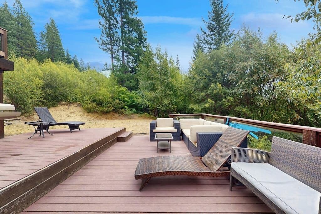 Une terrasse en bois, agréée de mobilier d’extérieur, notamment d’un canapé et de fauteuils, et entourée d’une végétation luxuriante.