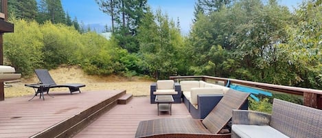 Une terrasse en bois, agréée de mobilier d’extérieur, notamment d’un canapé et de fauteuils, et entourée d’une végétation luxuriante.