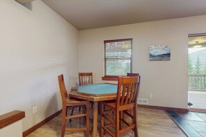 Un comedor con una mesa y sillas de madera, una ventana con persianas y un cuadro en la pared.