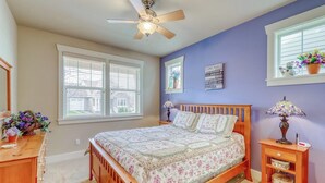 Een slaapkamer met een bed, een plafondventilator, een dressoir en een raam met jaloezieën.