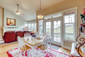 A dining area with a wooden table and white chairs, a red sofa, and a view through large windows. - Downtown 2BR - Fireplace - Patio (Sequim)
