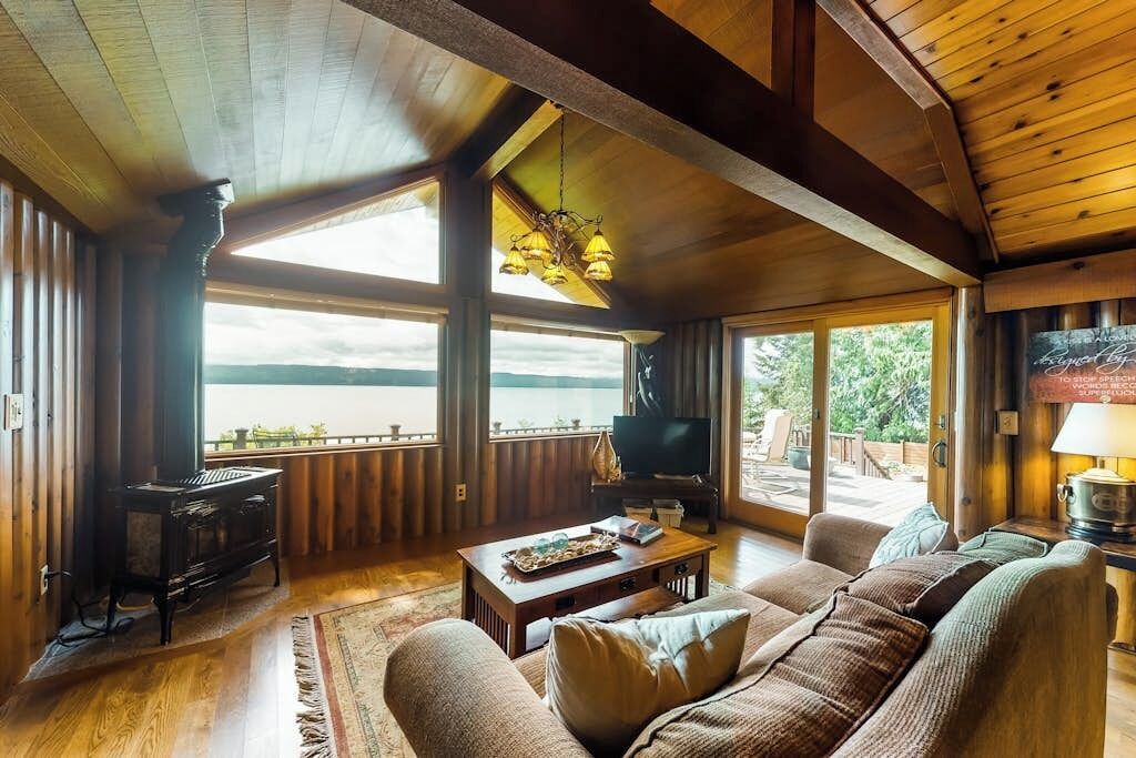 A spacious living room with a large window, wooden furniture, and a television.