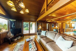 A cozy living room with a large sofa, a flat-screen TV, and a wooden ceiling. - 2BR waterfront home with full kitchen & deck views (Poulsbo)