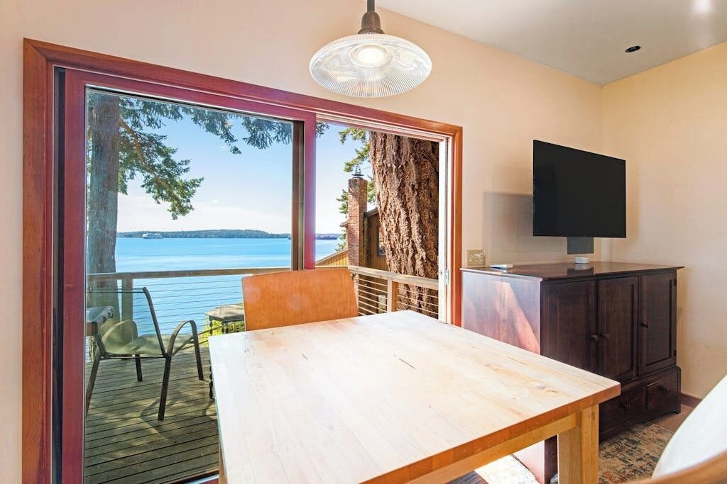A room with a large window, a wooden table, a television, and a cabinet.