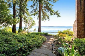 A pathway leading to a beach with tall trees and a brick building. - Studio Soundview Dog Friendly - WoodStove - Deck (Bainbridge Island)