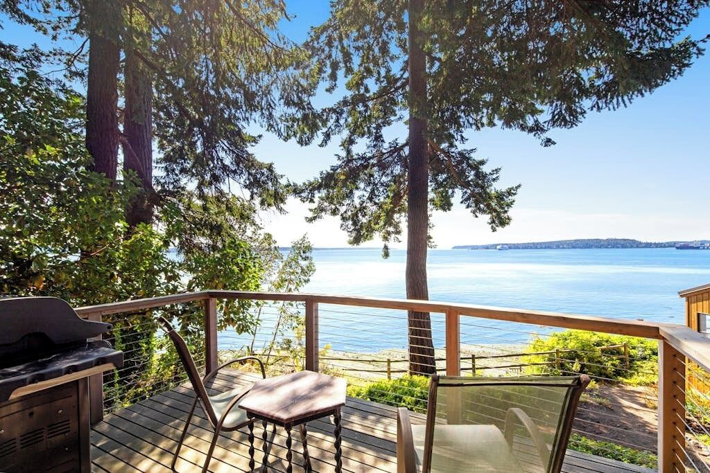 Een terras met een barbecue, stoelen en uitzicht op een meer.