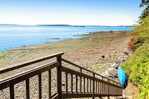 A wooden staircase leading down to a rocky shoreline with a view of the sea. - Studio Soundview Dog Friendly - WoodStove - Deck (Bainbridge Island)