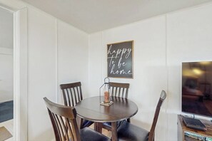 A dining area with a round table, four chairs, a candle holder, and a wall-mounted sign that reads 'happy to be home.' - 1BR Home in the Historic Marina District -1 dog ok (Westport)