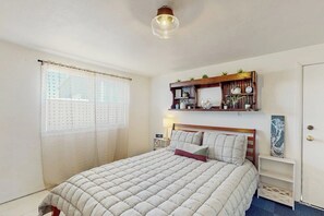 Ein Schlafzimmer mit einem Bett, einem Nachttisch, einem Regal mit Dekoration und einem Fenster mit Vorhängen.