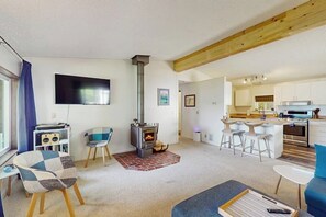 A living room with a fireplace, a TV, and a kitchen area with bar stools. - 2 BR water view house, dog friendly amenities (Belfair)