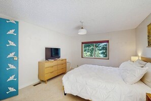 A bedroom with a bed, a dresser, a television, a window with a view of trees, and a blue door with white bird designs. - 2 BR water view house, dog friendly amenities (Belfair)