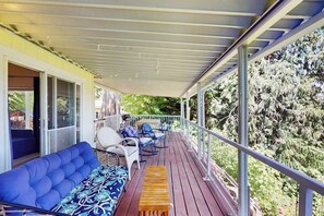 A covered deck with a sofa, chairs, and a table, overlooking a forested area. - 2 BR water view house, dog friendly amenities (Belfair)