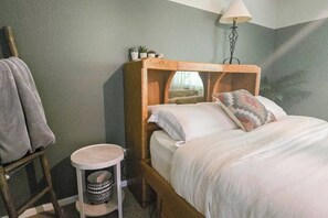 Ein Schlafzimmer mit einem hölzernen Kopfende, einem Nachttisch mit einer Lampe, einem kleinen Hocker und einem Bett mit Kissen.