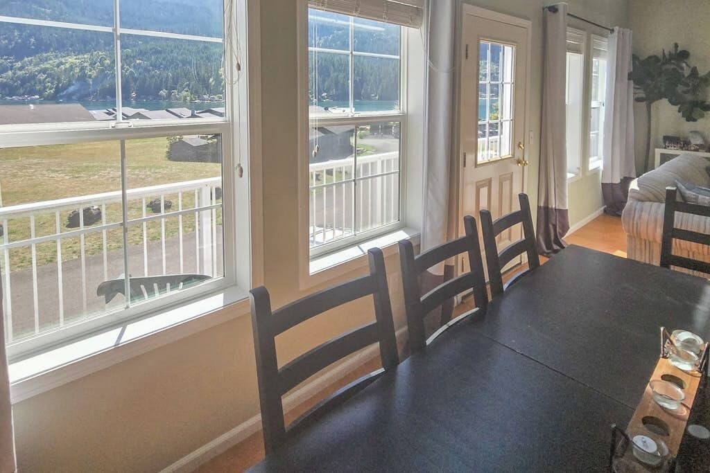 A dining area with a table and chairs, large windows with a view of a mountainous landscape, and a balcony with a railing.