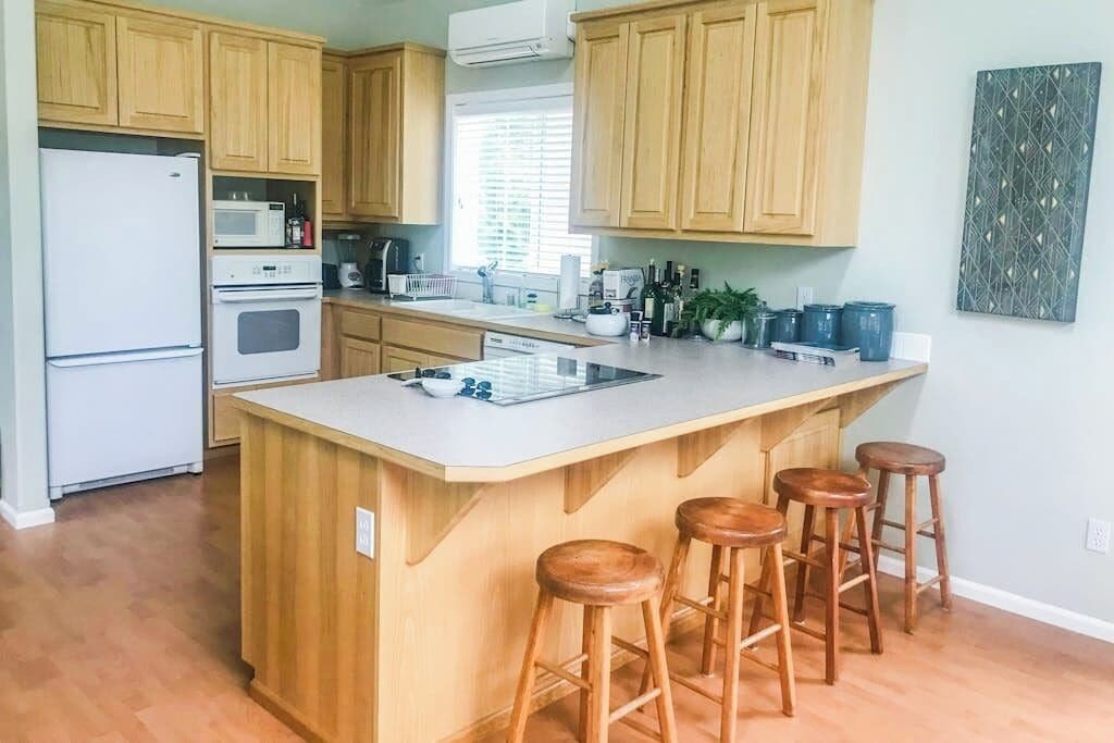 A kitchen with wooden cabinets, a white refrigerator, a microwave, a stove, a sink, and a bar area with stools.