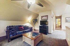 A living room with a sofa, a coffee table, a television, and a ceiling fan. - 2BR Cozy cabin getaway with firepit, and patio (Hoodsport)