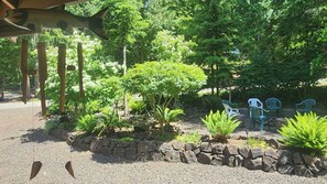 Un jardín con borde de piedra, plantas verdes y mobiliario exterior.