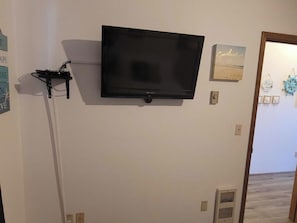 A room with a mounted television, a wall-mounted air conditioning unit, and a door leading to another space. - Oceanfront, dog-friendly 1BR with prime location (Ocean Shores)