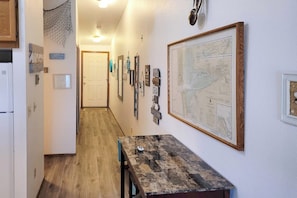 A hallway with a wooden floor, a table with a stone top, and various framed items on the walls. - Oceanfront, dog-friendly 1BR with prime location (Ocean Shores)