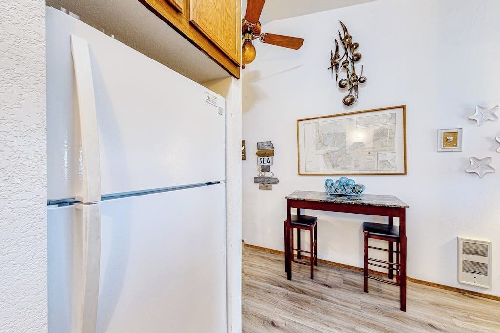 Una cocina con refrigerador blanco, ventilador de techo de madera, una mesa con dos sillas y decoración en la pared.
