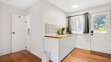 Quarto com piso de madeira, paredes brancas, painel de azulejos, janela com cortinas e uma porta.